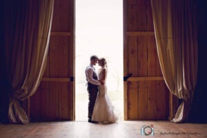 Bride and groom standing in between doors at their barn wedding at Port Farms