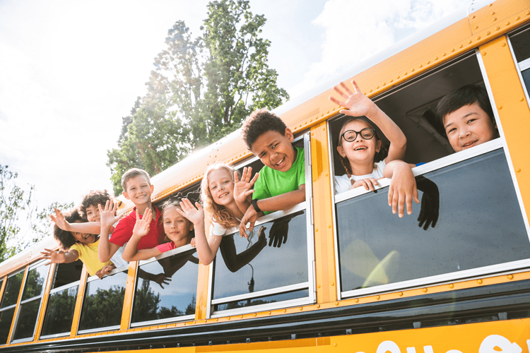 Students waving out the windows of a school bus.