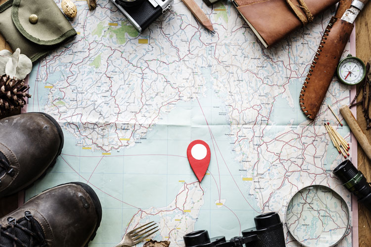 Red map marker on a map surrounded by various traveling items.